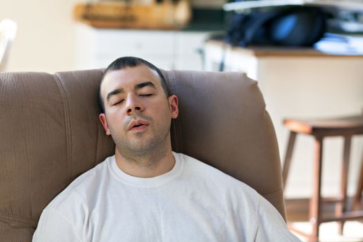 Lazy or overtired man sleeping on the couch in the seated position. Shallow depth of field.