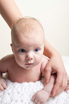 A cute newborn baby boy on a white blanket laying on his belly with mothers arm around him.