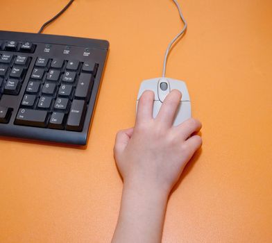 Children's right hand on a gray computer mouse on orange table