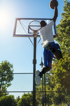 Young basketball player drives to the hoop with a high flying slam dunk. Slight lens flare.