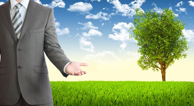 Businessman in suit holds her hand front of him. Tree and green landscape as backdrop