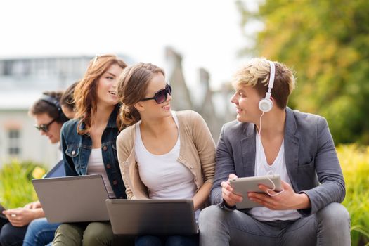 summer, internet, education, campus and teenage concept - group of students or teenagers with laptop and tablet computers hanging out