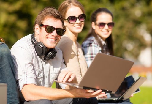 summer, internet, education, campus and teenage concept - group of students or teenagers with laptop and tablet computers hanging out