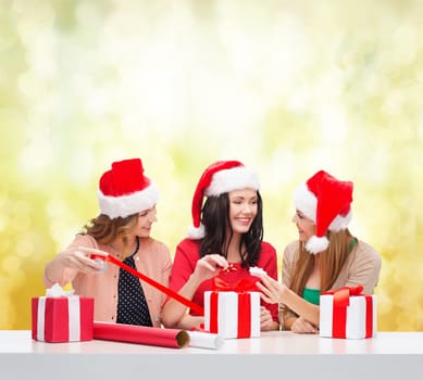 christmas, x-mas, winter, happiness concept - three smiling women in santa helper hats with gift boxes