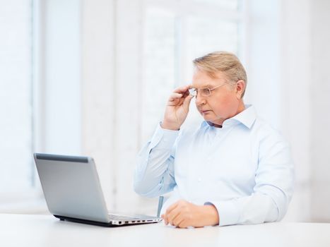 technology, oldness and lifestyle concept - old man in eyeglasses working with laptop computer at home