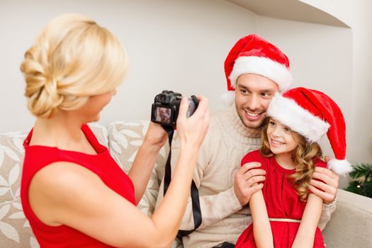family, christmas, x-mas, winter, happiness and people concept - mother taking picture of smiling father and daughter in santa helper hats