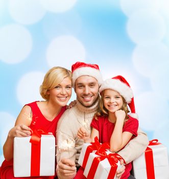 family, christmas, x-mas, winter, happiness and people concept - smiling family in santa helper hats with many gift boxes and bengal lights