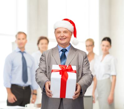 business, christmas, xmas, happiness concept - smiling old man in suit and santa helper hat with gift