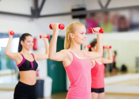 fitness, sport, training, gym and lifestyle concept - group of smiling women working out with dumbbells in the gym