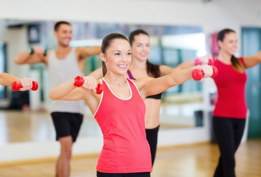 fitness, sport, training, gym and lifestyle concept - group of smiling people working out with dumbbells in the gym