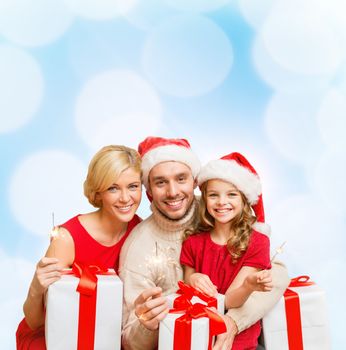 family, christmas, x-mas, winter, happiness and people concept - smiling family in santa helper hats with many gift boxes and bengal lights