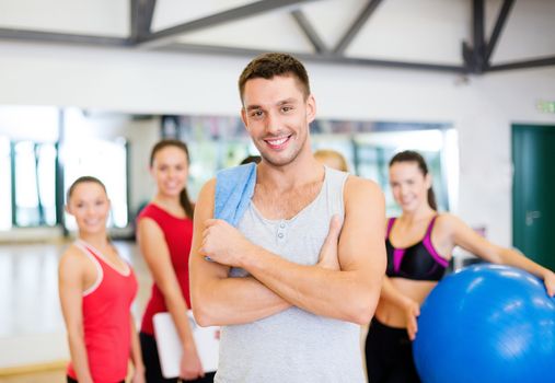 fitness, sport, training, gym and lifestyle concept - smiling man standing in front of the group of people in gym