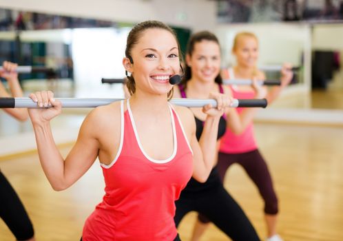 fitness, sport, training, gym and lifestyle concept - smiling trainer in front of the group of people working out with barbells in the gym