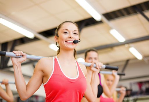 fitness, sport, training, gym and lifestyle concept - smiling trainer in front of the group of people working out with barbells in the gym