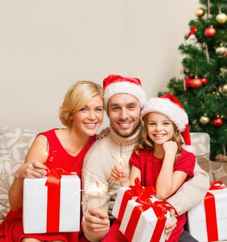 family, christmas, x-mas, winter, happiness and people concept - smiling family in santa helper hats with many gift boxes and bengal lights