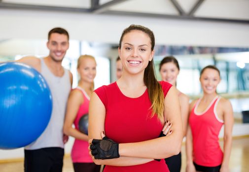 fitness, sport, training, gym and lifestyle concept - smiling woman standing in front of the group of people in gym