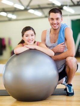 fitness, sport, training, gym and lifestyle concept - two smiling people with fitness ball in the gym