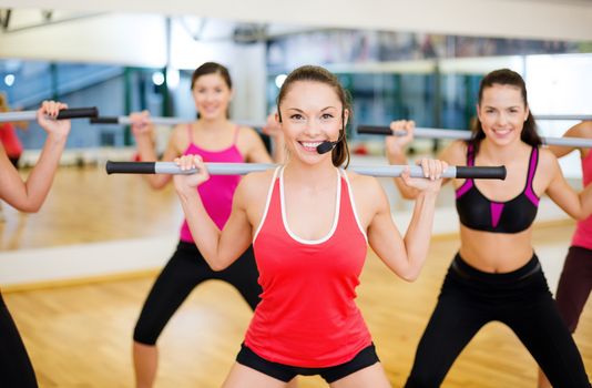 fitness, sport, training, gym and lifestyle concept - smiling trainer in front of the group of people working out with barbells in the gym