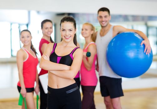 fitness, sport, training, gym and lifestyle concept - smiling woman standing in front of the group of people in gym