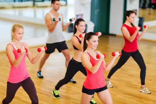 fitness, sport, training, gym and lifestyle concept - group of smiling people working out with dumbbells in the gym