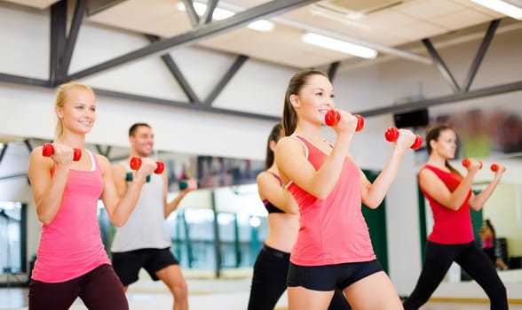 fitness, sport, training, gym and lifestyle concept - group of smiling people working out with dumbbells in the gym