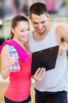 fitness, sport, training, gym and lifestyle concept - smiling male trainer with clipboard and woman with water bottle in the gym