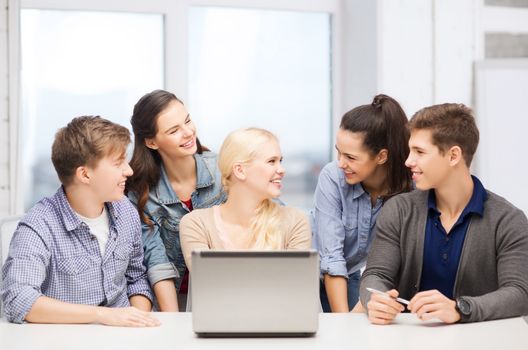 education, technology and internet concept - smiling students with laptop at school looking at each other