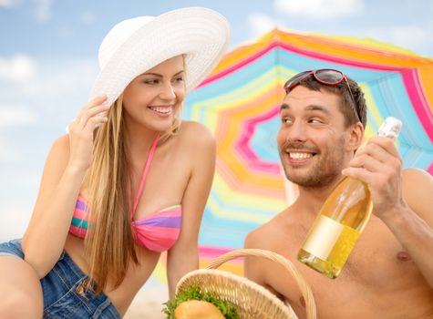 summer, holidays, vacation and happy people concept - smiling couple having picnic on the beach under colorful umbrella