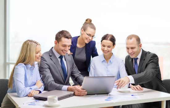 business, technology and office concept - smiling business team with laptop computers, documents and coffee having discussion in office