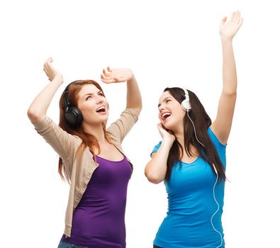 music and technology concept - two laughing teenagers with headphones dancing