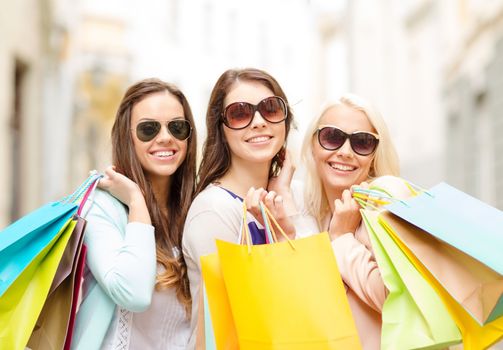 shopping, sale, happy people and tourism concept - three beautiful girls in sunglasses with shopping bags in ctiy