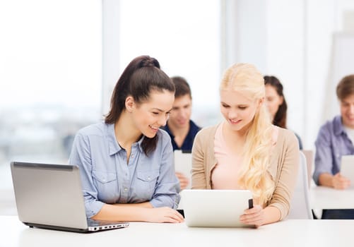 education, technology and internet concept - two smiling students with laptop computer, tablet pc and notebooks at school