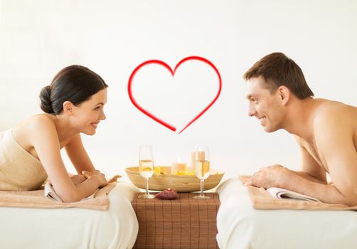 spa, beauty, love and happiness concept - smiling couple with candles in spa salon drinking champagne