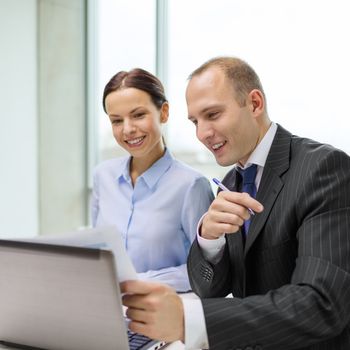 business, technology and office concept - businessman and businesswoman with laptop computer and papers having discussion in office