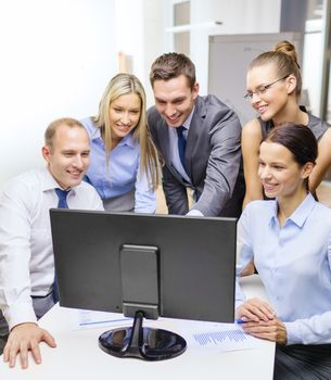 business, technology and office concept - smiling business team with computer monitor having discussion in office