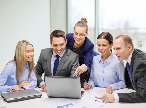 business, technology and office concept - smiling business team with laptop computers, documents and coffee having discussion in office