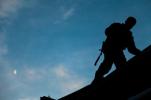 Contractor in Silhouette working on a Roof Top with blue Sky in Background