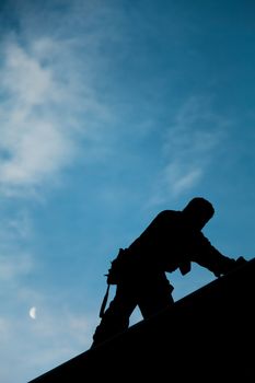 Contractor in Silhouette working on a Roof Top with blue Sky in Background