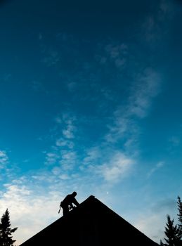 Contractor in Silhouette working on a Roof Top with blue Sky in Background