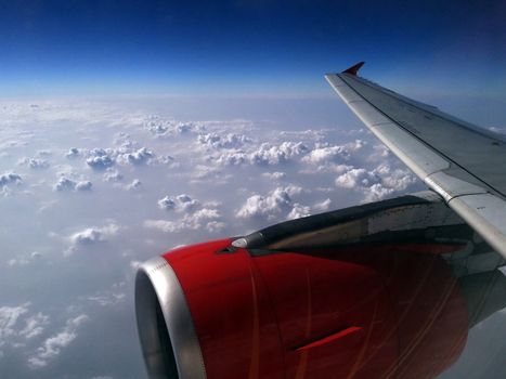 Deep blue sky and the farawy horizon form a frame for the grand view of clouds seen through the airplane window with engine and wing visible