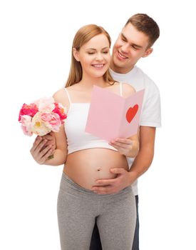 pregnancy, parenthood and happiness concept - happy young family expecting child with pink postcard and flowers