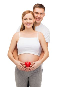 pregnancy, parenthood, love and happiness concept - happy young family expecting child with small red heart