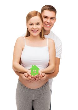 pregnancy, parenthood, real estate and happiness concept - happy young family expecting child showing green paper house