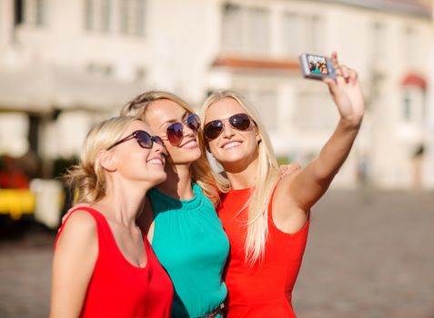 holidays, tourism and modern technology concept - three beautiful girls taking picture with digital camera in the city