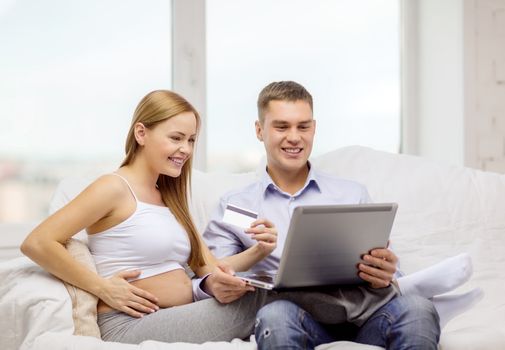 pregnancy, parenthood, internet, banking, money and technology concept - expecting family with laptop computer and credit card