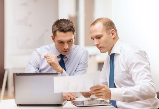 business, technology and office concept - two businessmen with laptop, tablet pc computer and papers having discussion in office