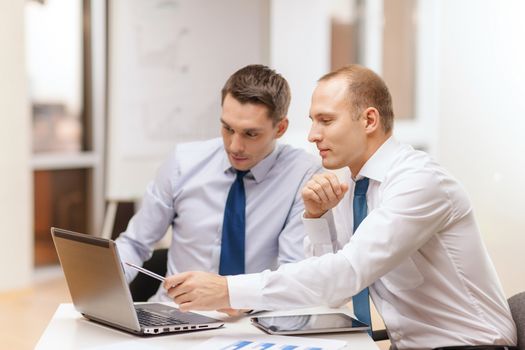 business, technology and office concept - two businessmen with laptop, tablet pc computer and papers having discussion in office