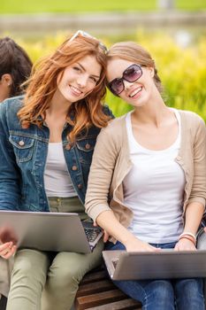 summer holidays, education, campus, technology and teenage concept - two female students with laptop computers