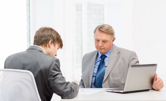 business, technology and office concept - older man and young man signing papers in office