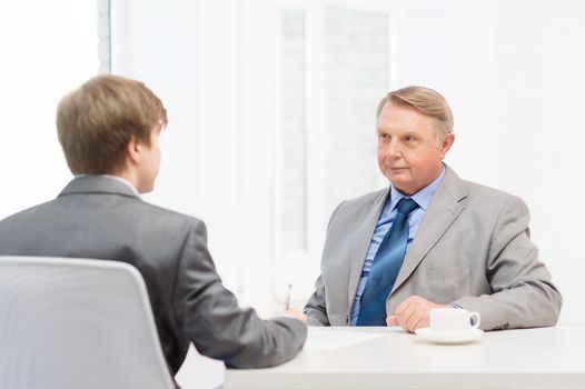 business, technology and office concept - older man and young man signing papers in office